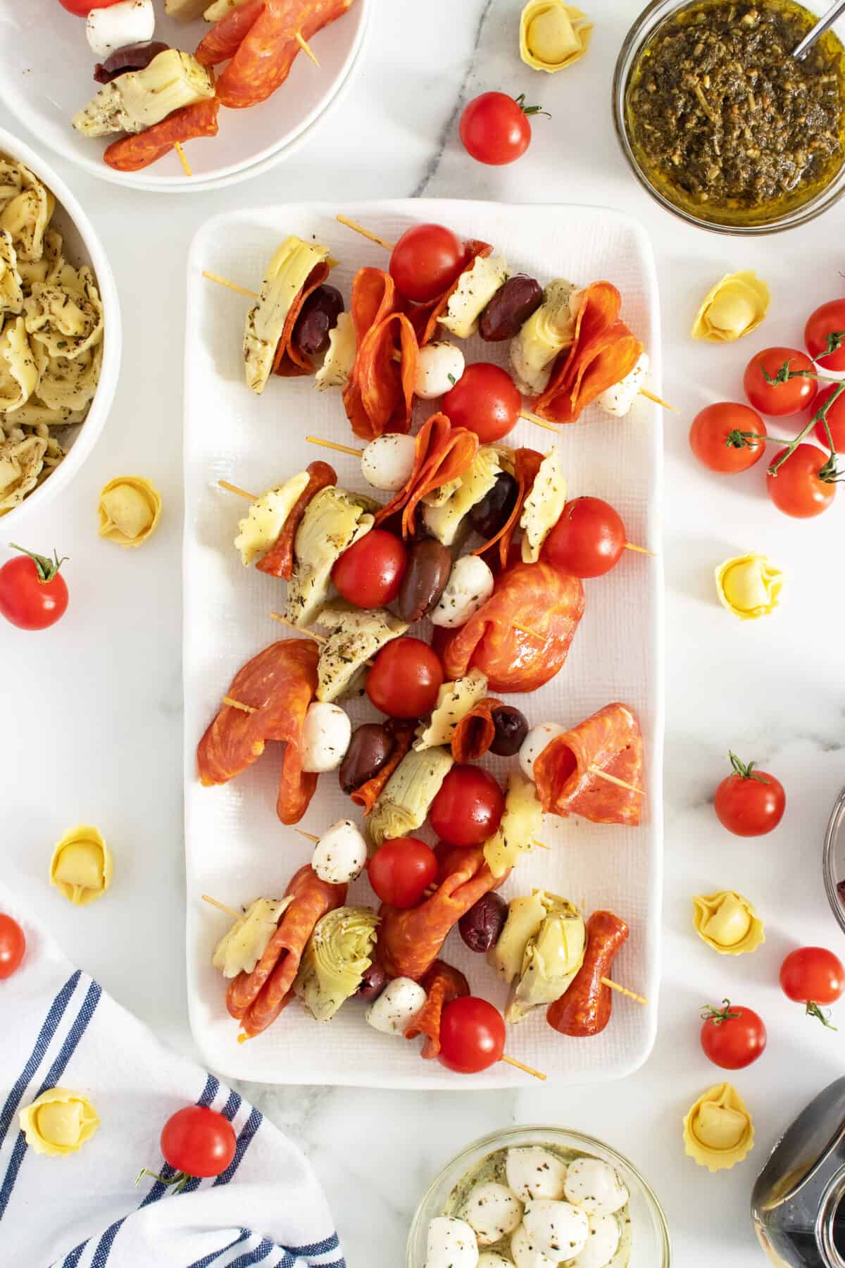 Serving a plate full of these antipasto skewers is an easy and delicious way to entertain your guests. Make them ahead of time and refrigerate, then serve. #thekitchenmagpie Antipasto skewers on a rectangle white platter