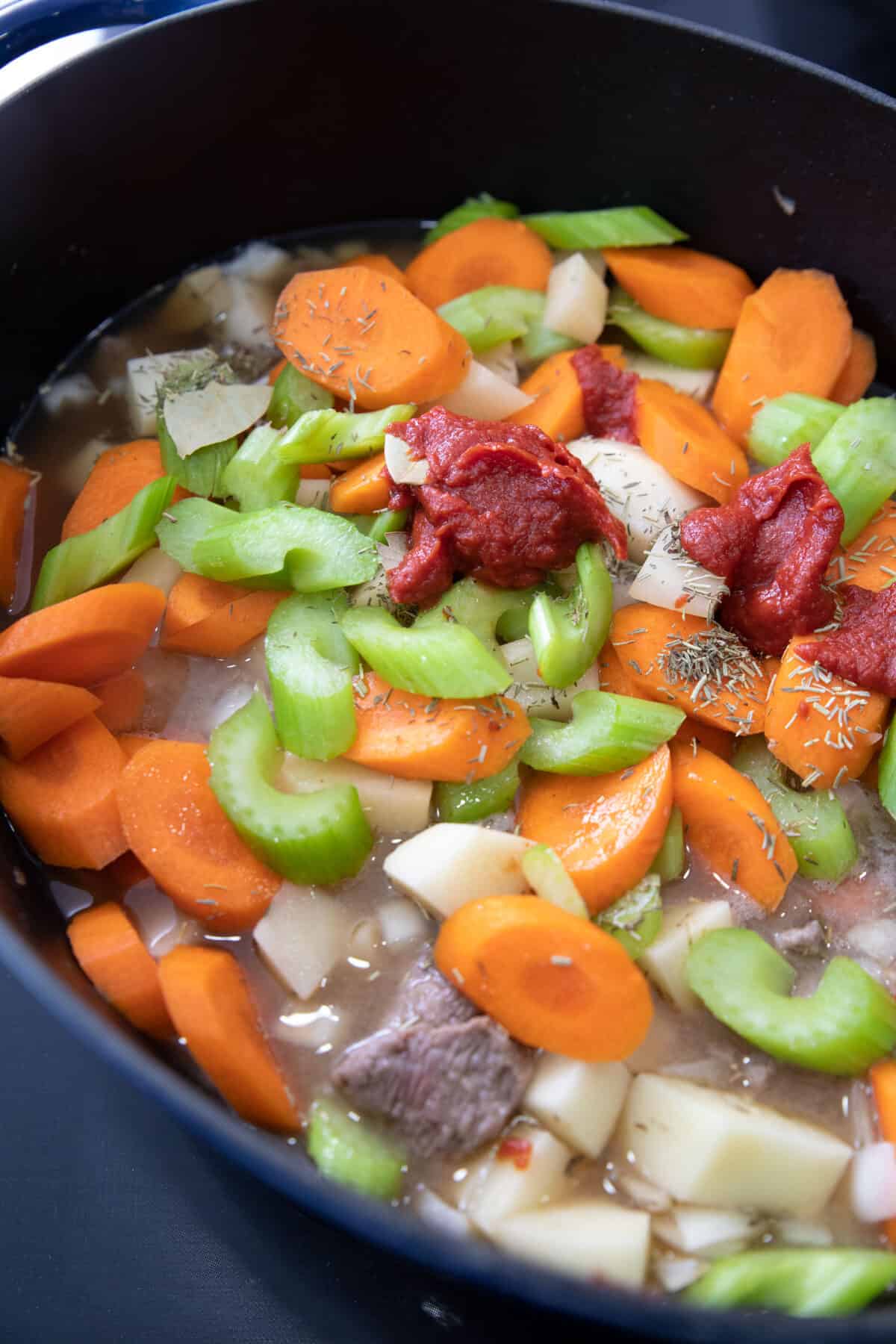 Make a delicious, tender beef stew that is simmered in a Dutch Oven for the best results.#thekitchenmagpie #easyrecipes #beefstew raw veggies and tomato sauce in a dutch oven