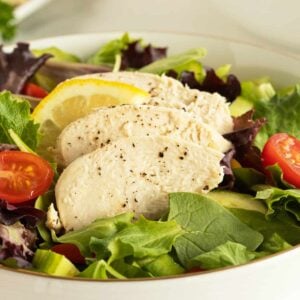 poached chicken in a bowl on top of lettuce and cherry tomatoes